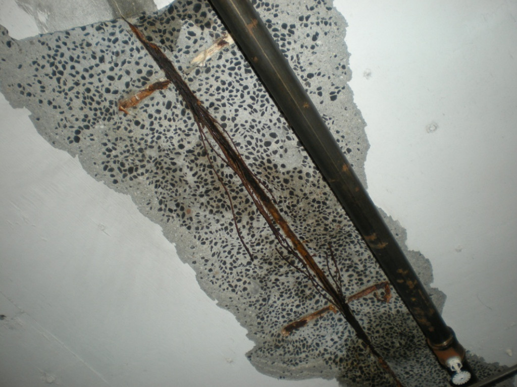 Severely corroded post tension tendon wires exposed in a concrete slab due to moisture infiltration, possibly caused by a nearby pipe leak.